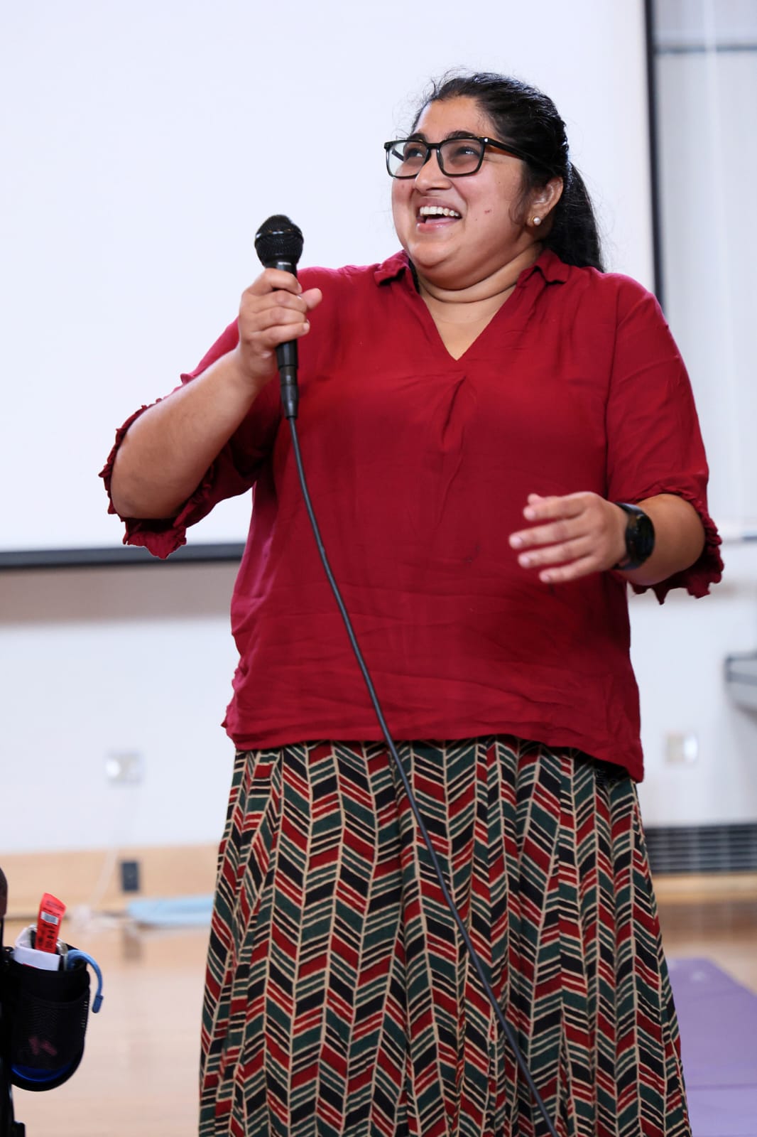 A dancer holding a microphone pauses mid-laugh, joy spilling into the moment as they stand against the clean light of the studio.