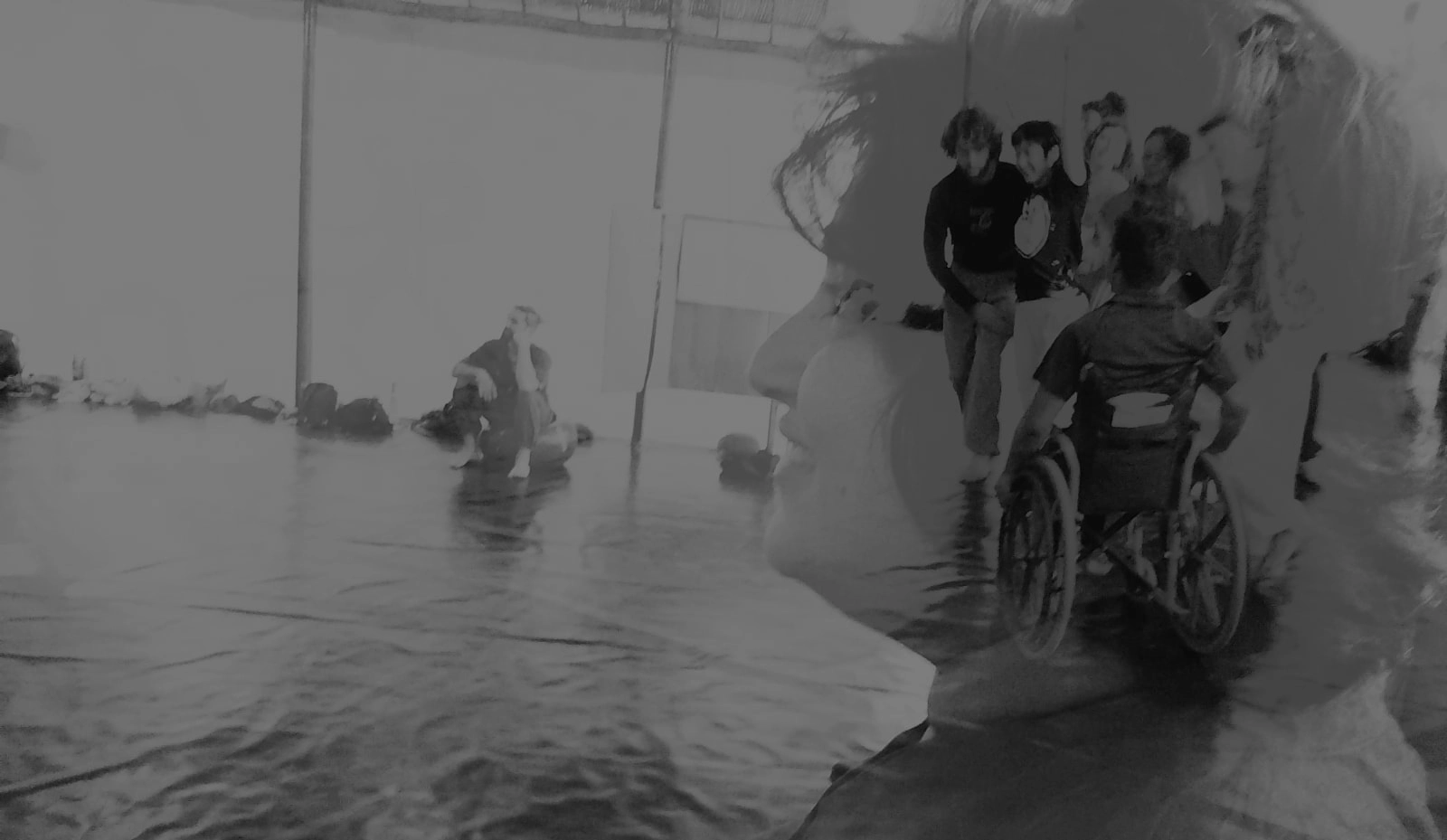 Double-exposed black-and-white photograph blending a close side profile of a woman with a scene inside a dance studio. In the overlaid studio image, several dancers—including a wheelchair dancer—rehearse across a wide marley floor. The two scenes merge so the dancers appear to be moving inside her head, suggesting that her mind is filled with dance, disability culture, and the possibilities of access.